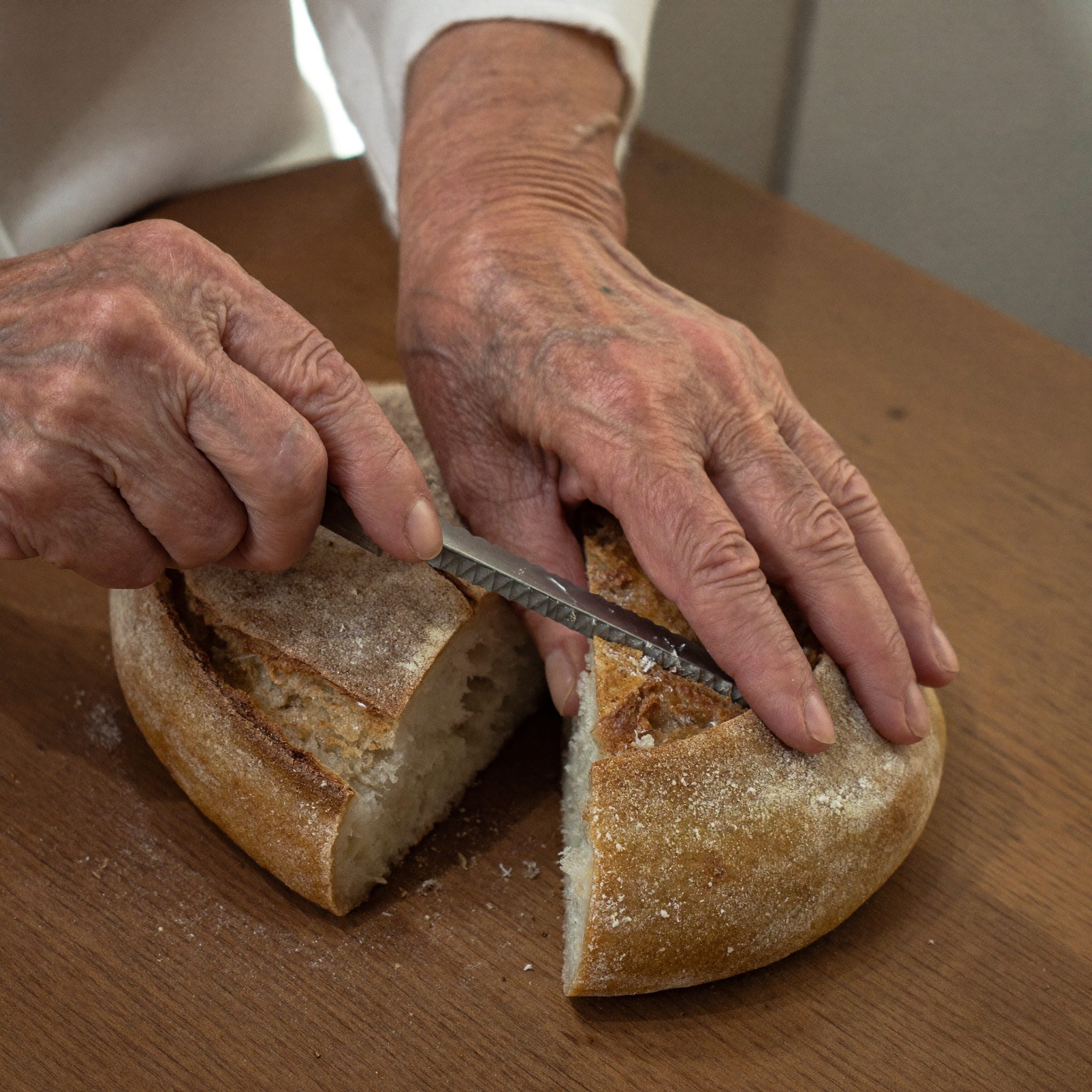Mãos de avó a partir pão caseiro para a açorda